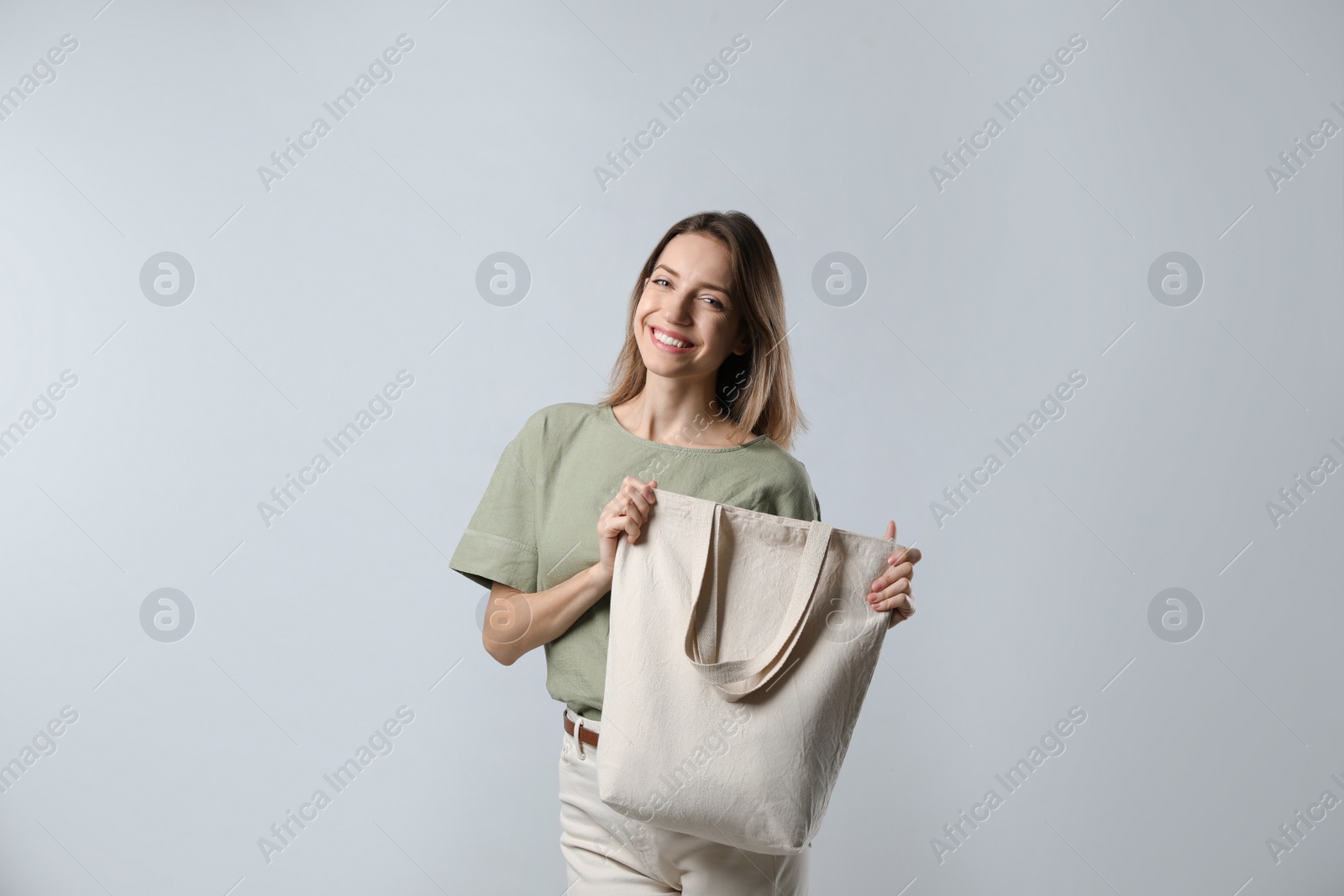 Photo of Happy young woman with blank eco friendly bag on light background