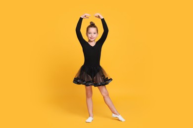Photo of Cute little girl in black dress dancing on yellow background
