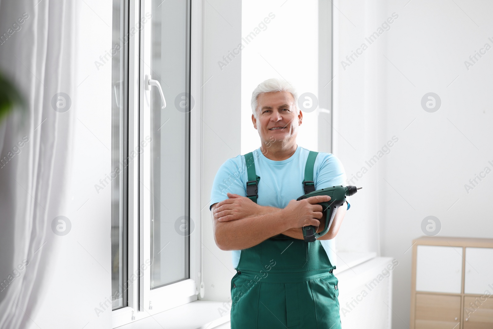 Photo of Mature repairman with electric screwdriver near plastic window indoors