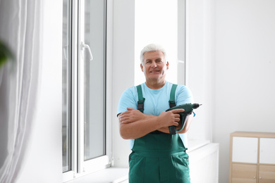 Photo of Mature repairman with electric screwdriver near plastic window indoors