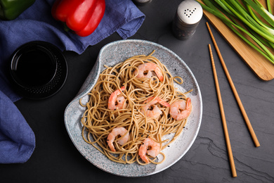 Photo of Tasty buckwheat noodles with shrimps served on black table, flat lay