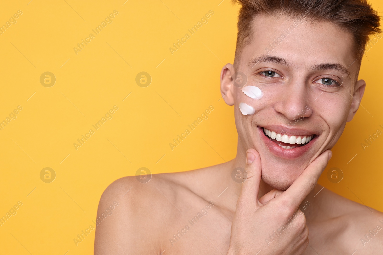 Photo of Handsome man with moisturizing cream on his face against orange background. Space for text