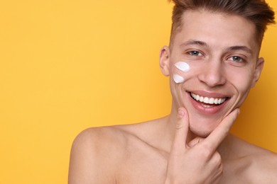 Handsome man with moisturizing cream on his face against orange background. Space for text