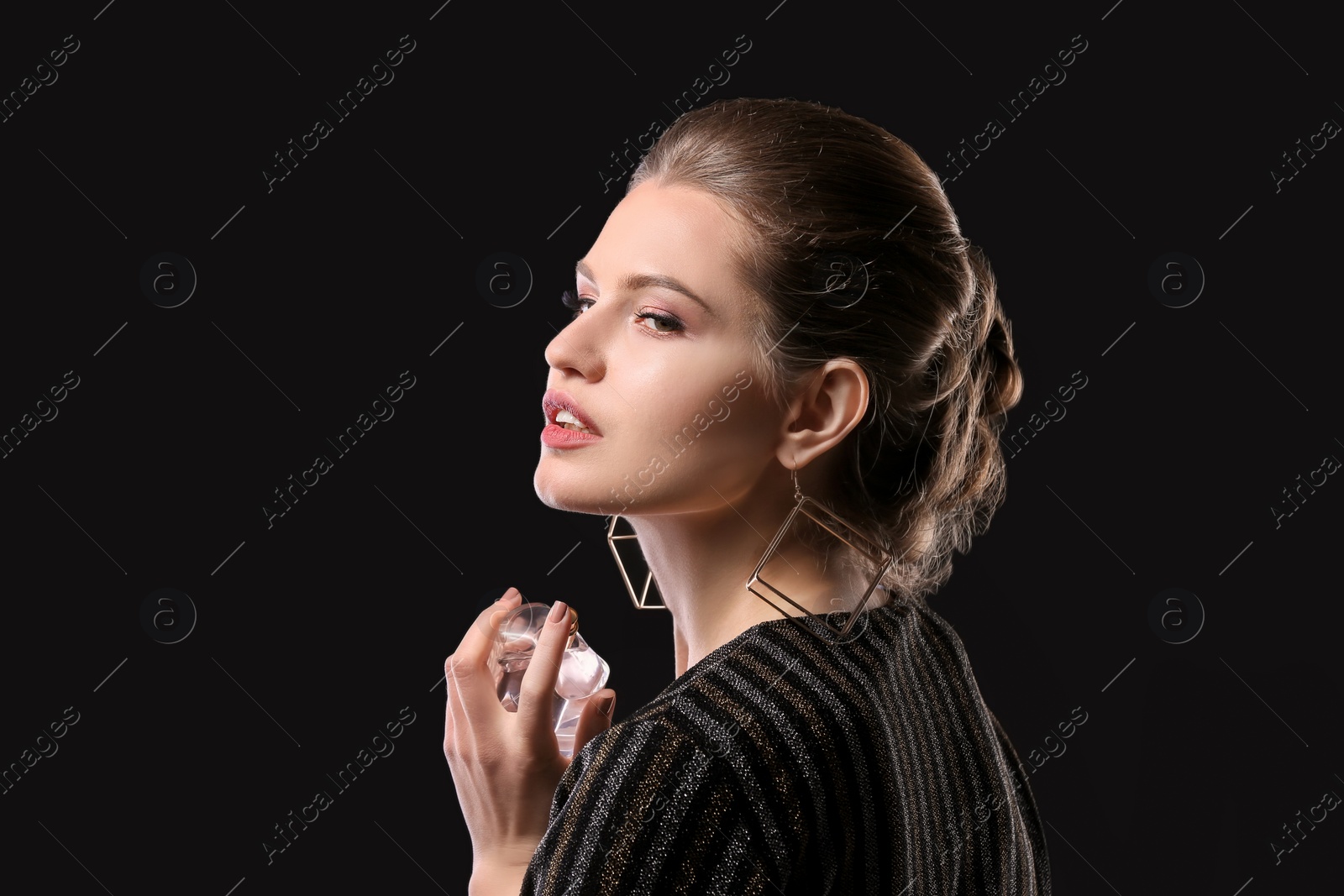 Photo of Beautiful young woman with bottle of perfume on black background