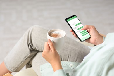 Woman texting via mobile phone while drinking coffee indoors, closeup. Device screen with messages