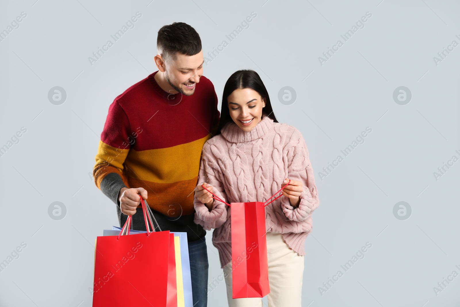 Photo of Happy couple with paper bags on grey background. Christmas shopping