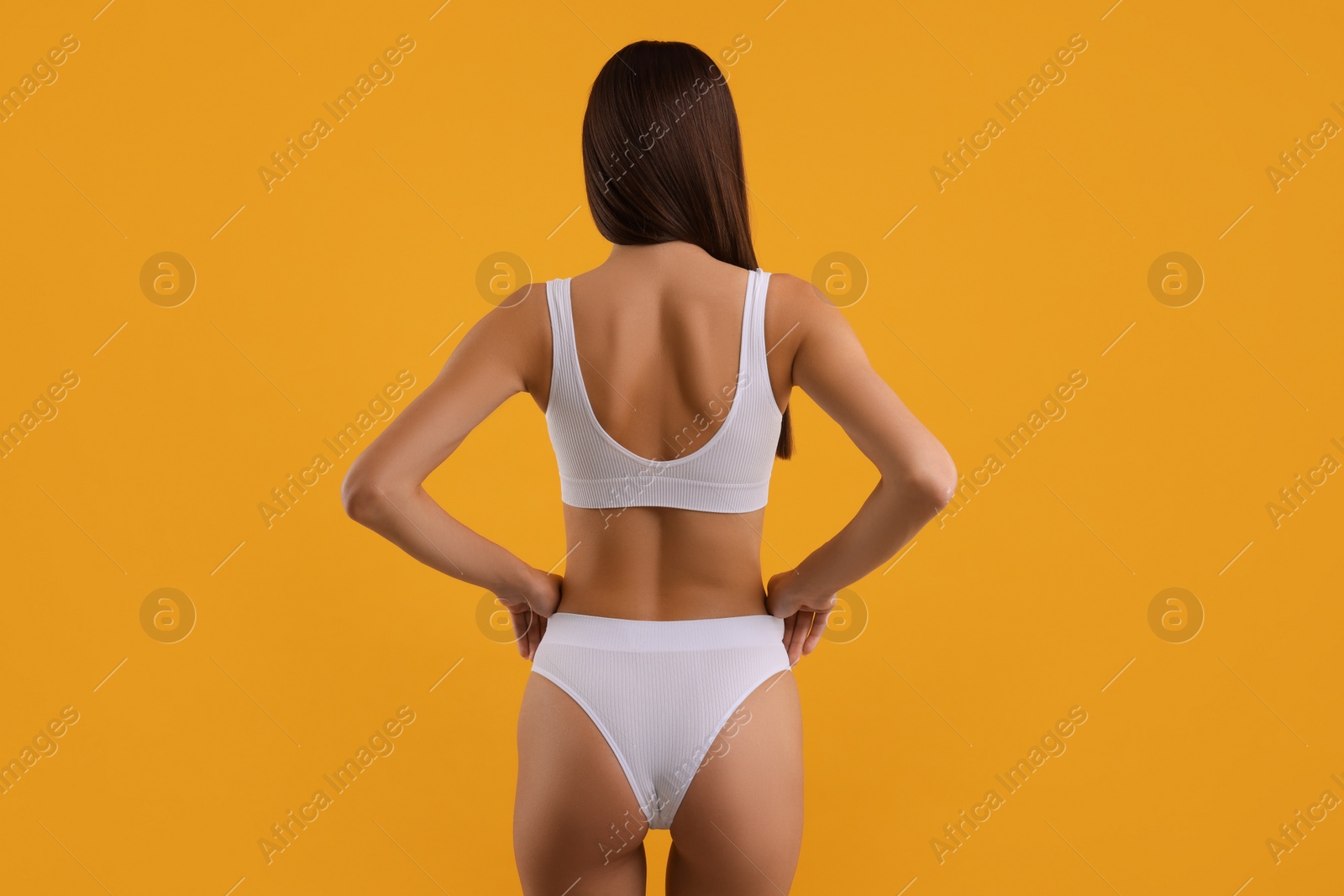 Photo of Young woman in stylish white bikini on orange background, back view