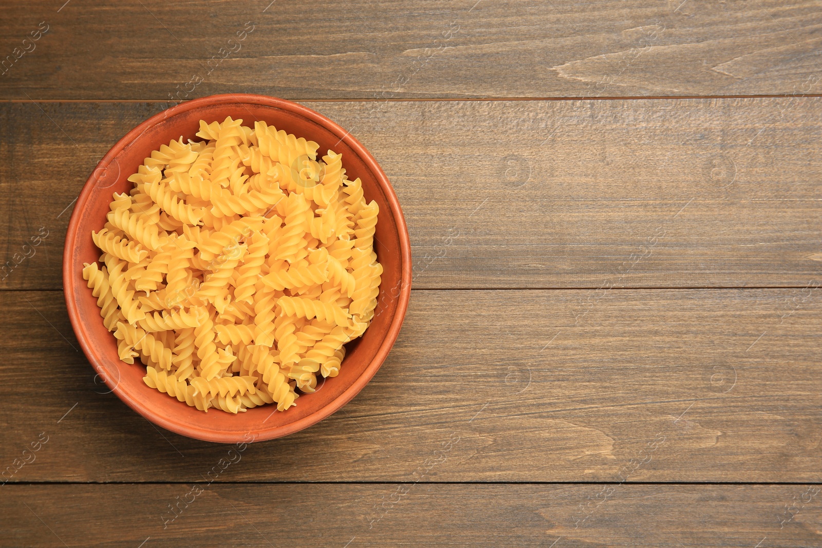 Photo of Raw fusilli pasta in bowl on wooden table, top view. Space for text