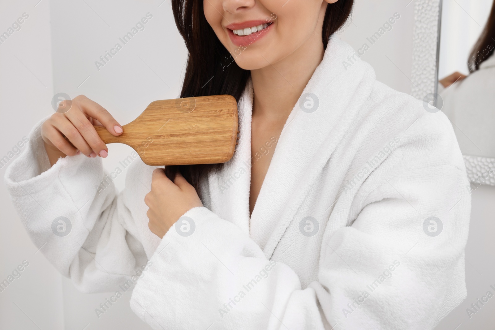 Photo of Beautiful woman brushing her hair indoors, closeup