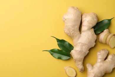 Photo of Fresh ginger with green leaves on pale light yellow background, flat lay. Space for text