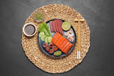 Photo of Tasty salmon slices, shrimp, cucumber and tuna on black table, top view. Delicious sashimi dish