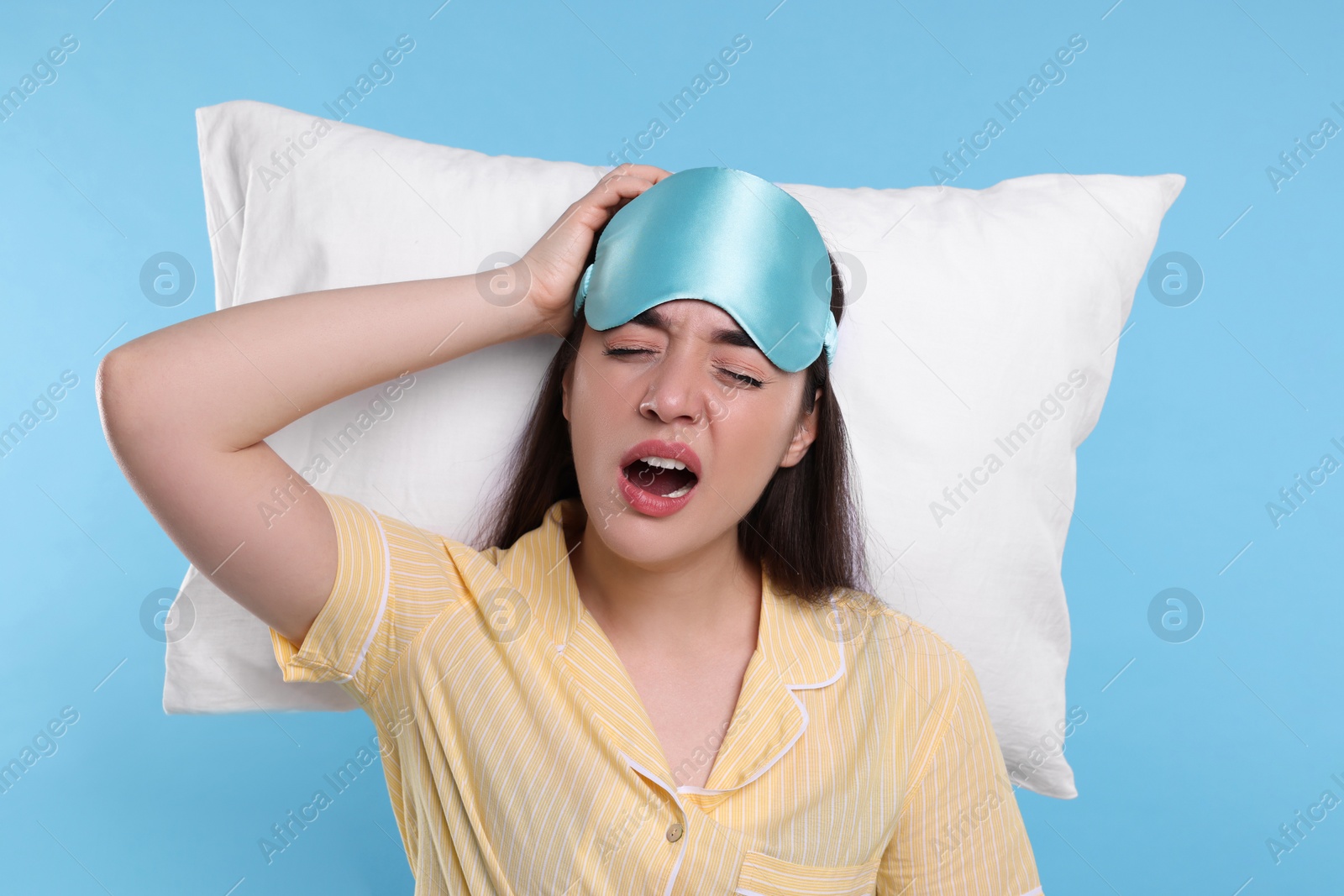 Photo of Tired young woman with sleep mask and pillow on light blue background. Insomnia problem