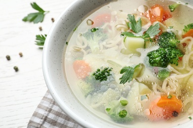 Bowl of fresh homemade vegetable soup on white wooden background, closeup