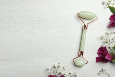 Natural jade face roller and flowers on light background, flat lay. Space for text