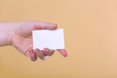 Man holding paper card on pale orange background, closeup. Mockup for design