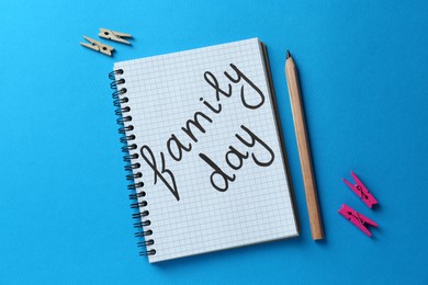 Photo of Notebook with text Family Day, pencil and decorative clothespins on light blue background, flat lay