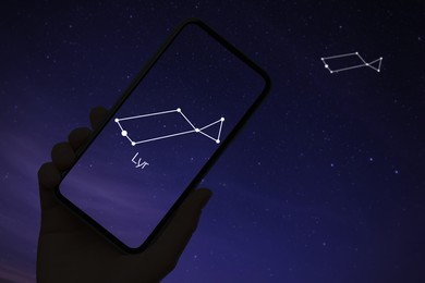 Image of Woman using stargazing app on her phone at night, closeup. Identified stick figure pattern of Lyra constellation on device screen