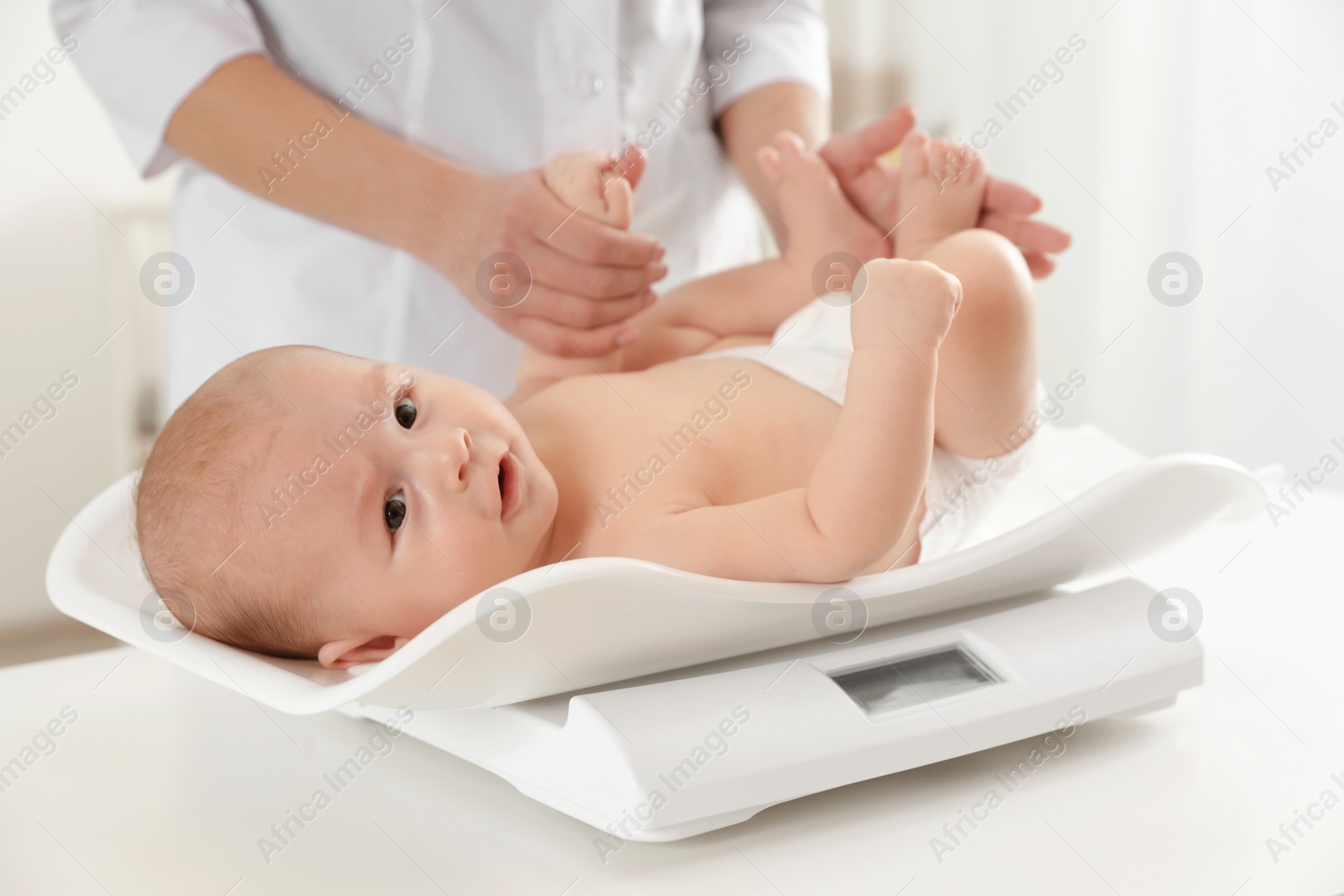 Photo of Doctor weighting baby on scales in light room