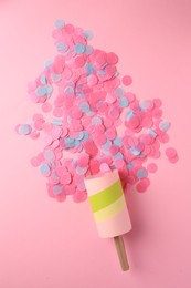 Colorful confetti bursting out of party popper on pink background, flat lay