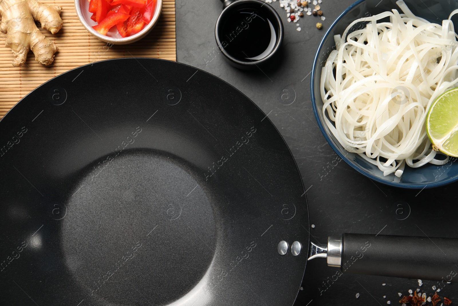 Photo of Flat lay composition with black wok, spices and products on dark table