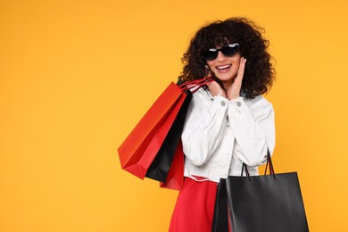 Photo of Happy young woman with shopping bags and stylish sunglasses on yellow background. Space for text