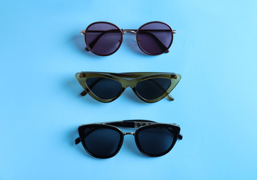 Photo of Many stylish sunglasses on light blue background, flat lay