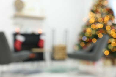 Beautiful Christmas tree near fireplace and cosy armchairs indoors, blurred view