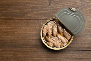 Open tin can of sprats on wooden table, top view. Space for text