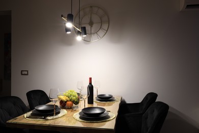 Photo of Table with plates, fruits, glasses and bottle of wine in room