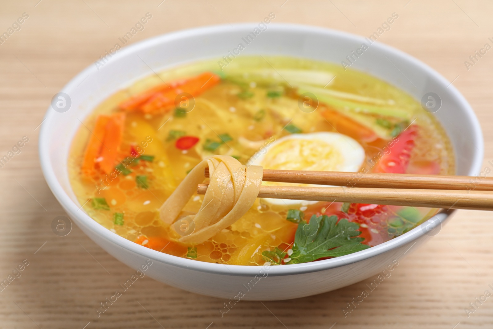 Photo of Chopsticks with noodles over bowl of tasty ramen on wooden table