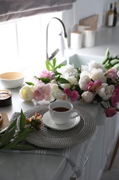 Beautiful peonies and cup of tea on kitchen counter