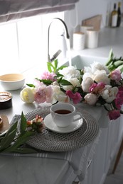 Photo of Beautiful peonies and cup of tea on kitchen counter