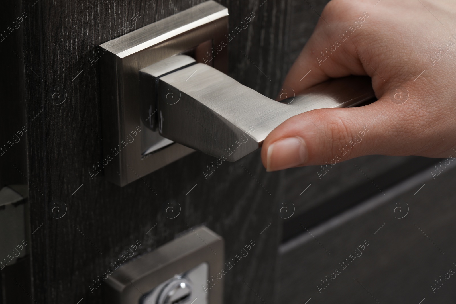 Photo of Woman opening wooden door indoors, closeup of hand on handle