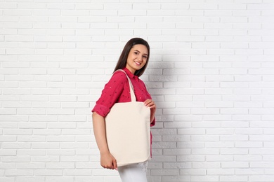 Beautiful young woman with stylish blank eco bag near brick wall, space for text