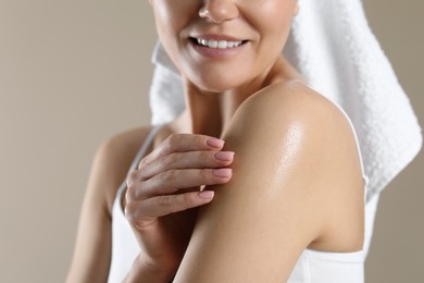 Photo of Woman applying body oil onto shoulder on beige background, closeup