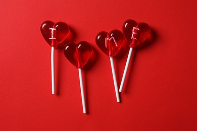 Photo of Phrase I Love Me made of heart shaped lollipops on red background, flat lay
