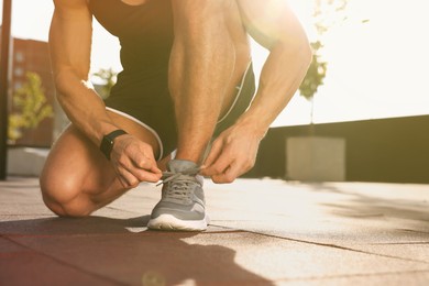 Photo of Man tying shoelaces before running outdoors on sunny day, closeup