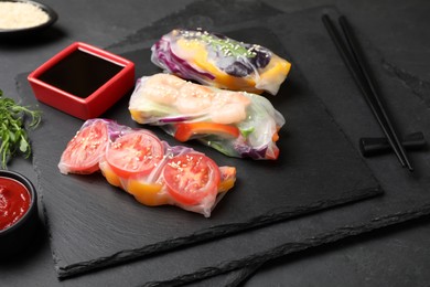 Delicious rolls wrapped in rice paper served on black table, closeup