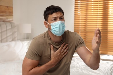 Photo of Man with medical mask suffering from pain during breathing in bedroom