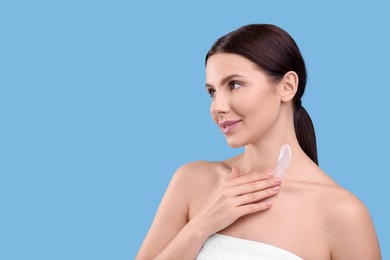 Photo of Beautiful woman with smear of body cream on her neck against light blue background, space for text