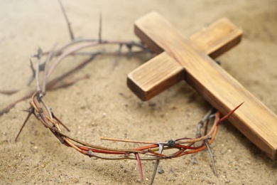 Photo of Crown of thorns and wooden cross on sand. Easter attributes