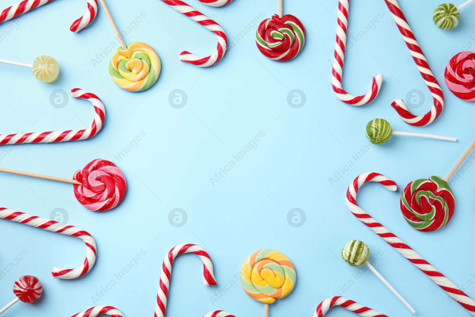 Photo of Flat lay composition with candy canes and lollipops on light blue background. Space for text