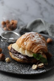 Delicious croissant with banana, chocolate and hazelnuts on grey table, closeup