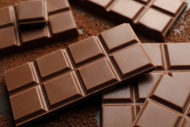 Photo of Delicious milk chocolate and cocoa powder on grey table, closeup