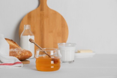 Photo of Jar with honey, milk, butter and bread served for breakfast on table. Space for text