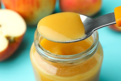 Photo of Spoon with healthy baby food over glass jar on turquoise table, closeup