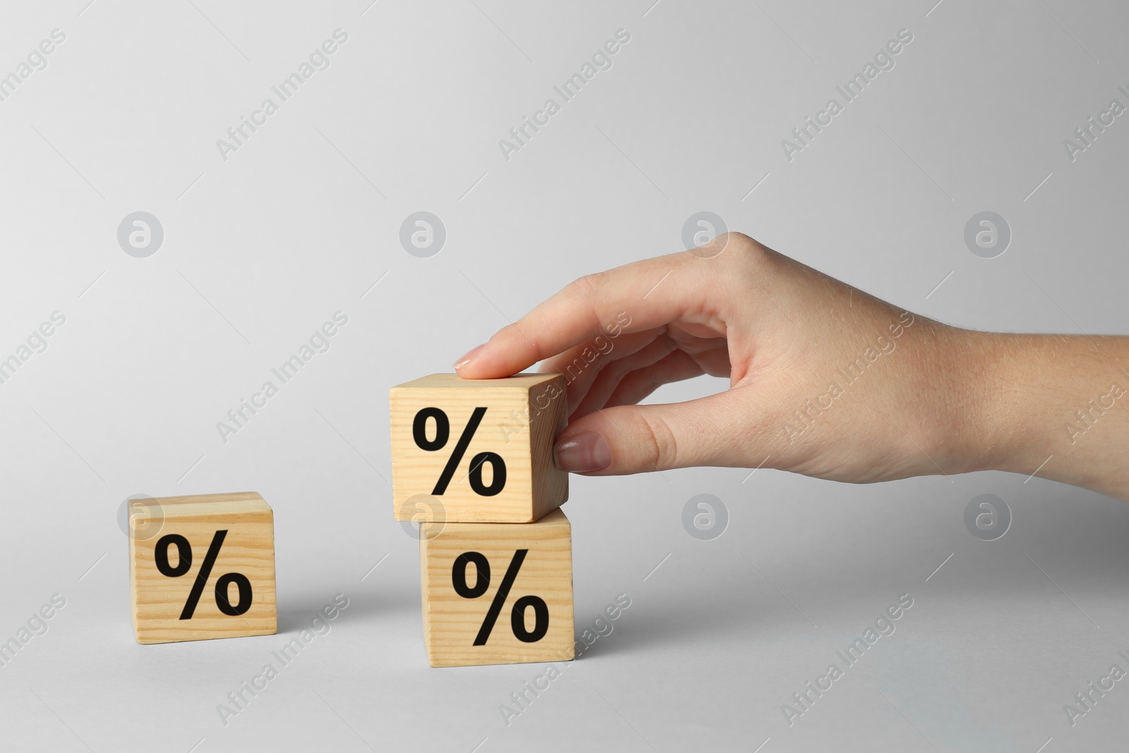 Photo of Woman stacking wooden cubes with percent signs on light background, closeup