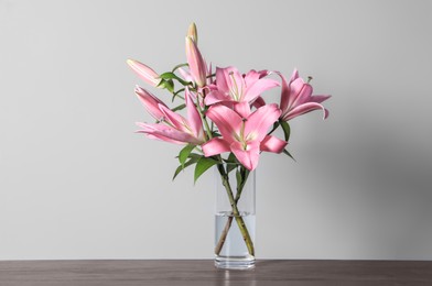 Beautiful pink lily flowers in vase on wooden table against light background