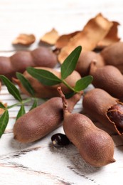 Photo of Delicious ripe tamarinds and leaves on white wooden table, closeup