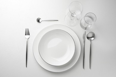 Photo of Stylish setting with cutlery and glasses on white textured table, flat lay